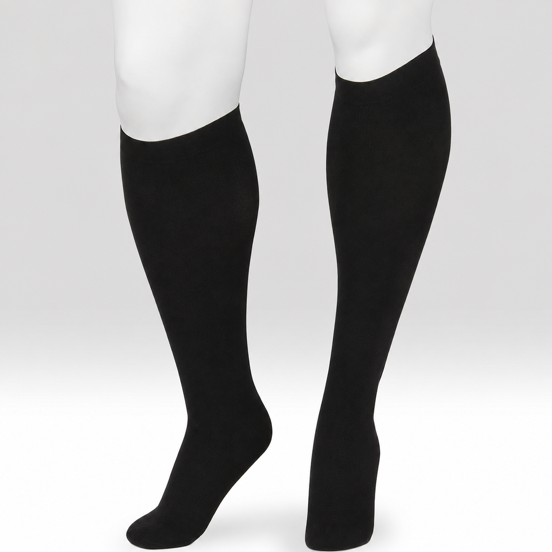 A pair of black knee-high compression socks or calf sleeves shown on a white mannequin lower leg and foot form against a light gray studio background. - okotoks hc pharmacy