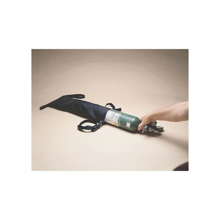 Hand holding a green oxygen tank with black carrying strap on a beige background - Okotoks HC Pharmacy