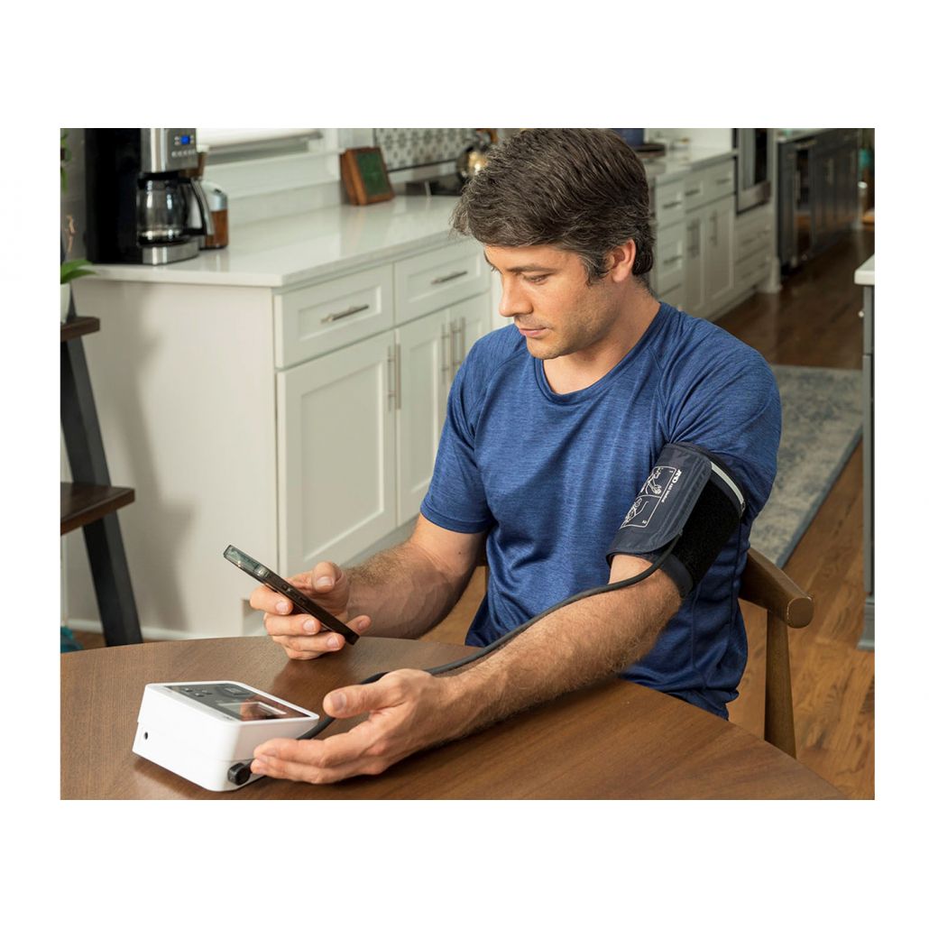 Man taking his blood pressure in a kitchen using a device and smartphone. - Okotoks HC Pharmacy