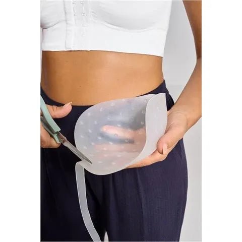 Person holding a silicone breast form with scissors on a plain background - okotoks hc pharmacy