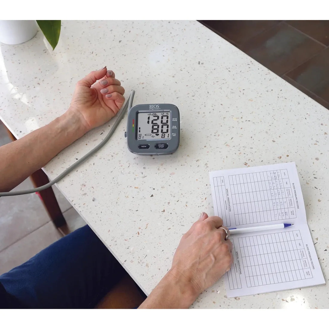 Person using a blood pressure monitor on a table with a notepad and pen. - okotoks hc pharmacy