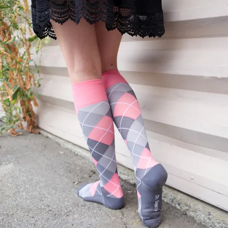 A person wearing knee-high argyle socks with pink, gray, and white diamonds, standing outdoors against a light wood siding wall. - okotoks hc pharmacy