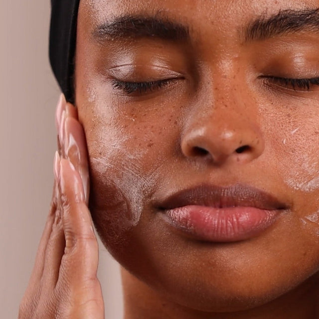 Close-up of a person applying skincare product to their face with a neutral background - okotoks hc pharmacy