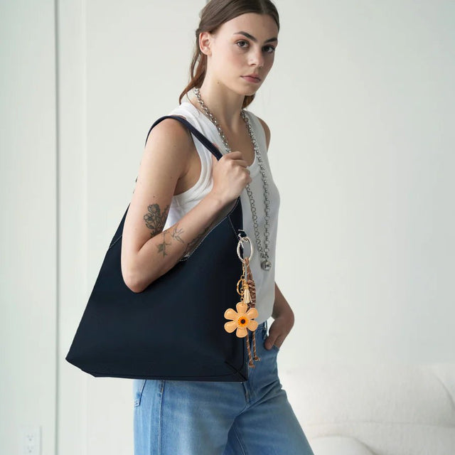 Woman holding a black bag with a floral keychain against a white background - okotoks hc pharmacy