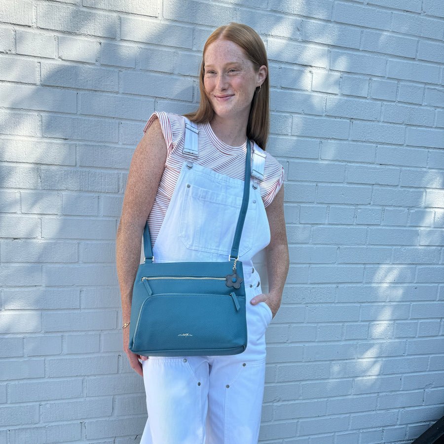 Woman holding a blue handbag against a light blue brick wall - okotoks hc pharmacy