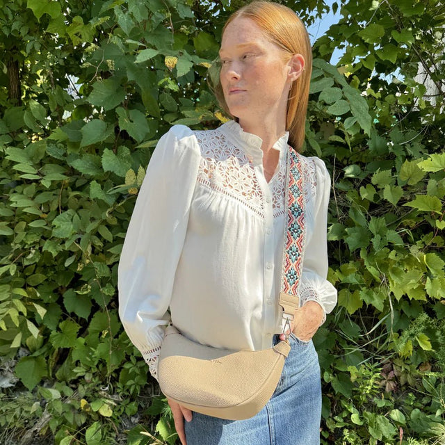 Woman wearing a white blouse with embroidery and blue jeans standing in front of green foliage. - okotoks hc pharmacy