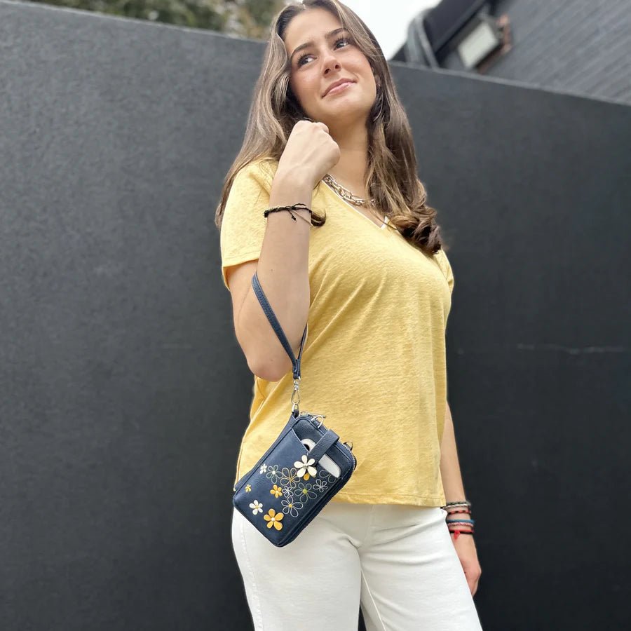 Woman wearing a yellow shirt and white pants with a blue floral purse against a black background - okotoks hc pharmacy