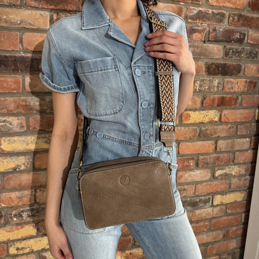 Person holding a brown crossbody bag against a brick wall - okotoks hc pharmacy