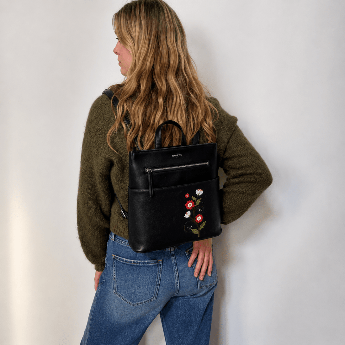 Person wearing a black backpack with floral embroidery against a white wall - okotoks hc pharmacy