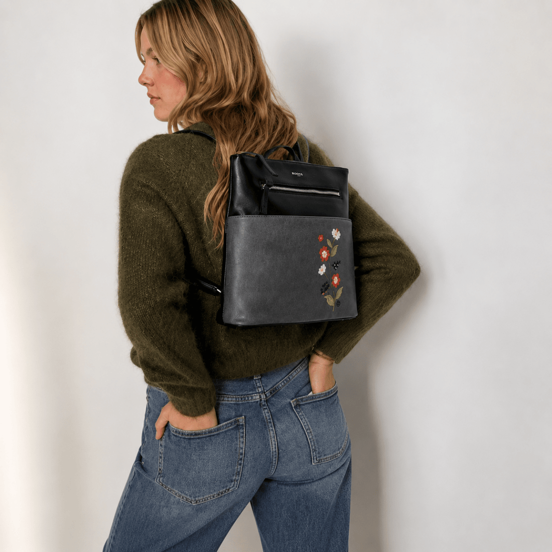 Person wearing a black backpack with floral embroidery on a plain background - okotoks hc pharmacy