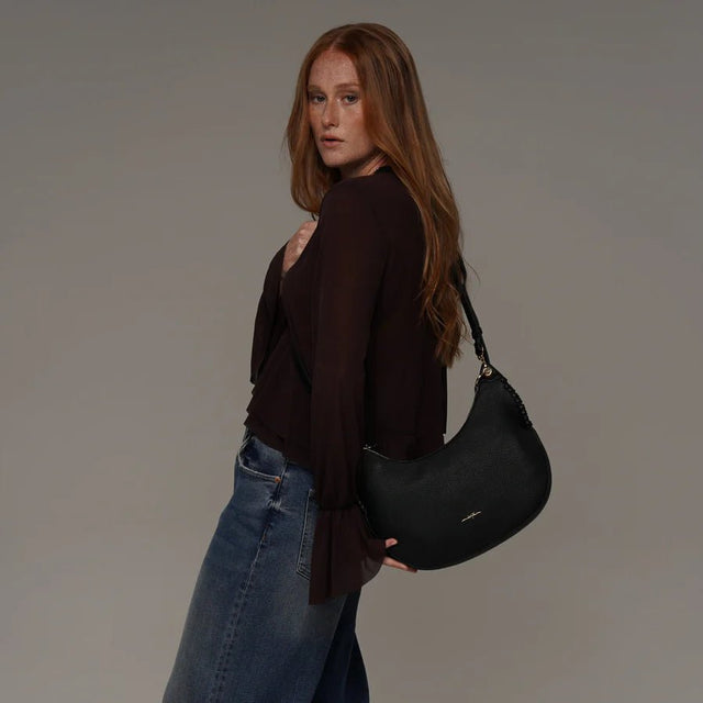Woman holding a black handbag against a plain background - okotoks hc pharmacy