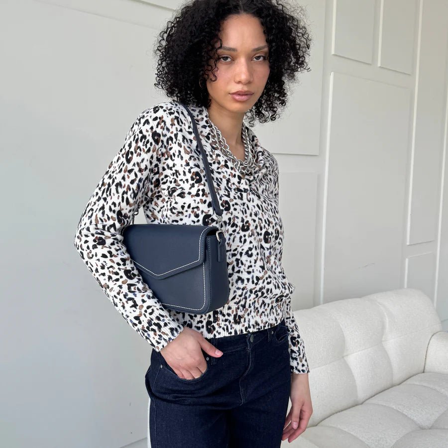 Woman wearing a leopard print shirt and holding a blue handbag in a room with a white couch. - okotoks hc pharmacy