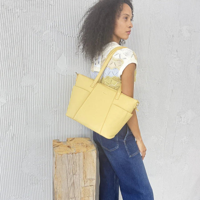 Woman holding a yellow tote bag against a textured gray wall. - okotoks hc pharmacy