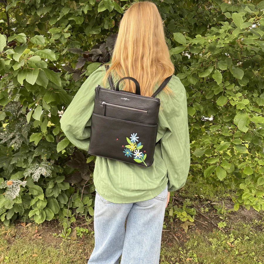 Person wearing a black backpack with floral embroidery in a green outdoor setting - okotoks hc pharmacy