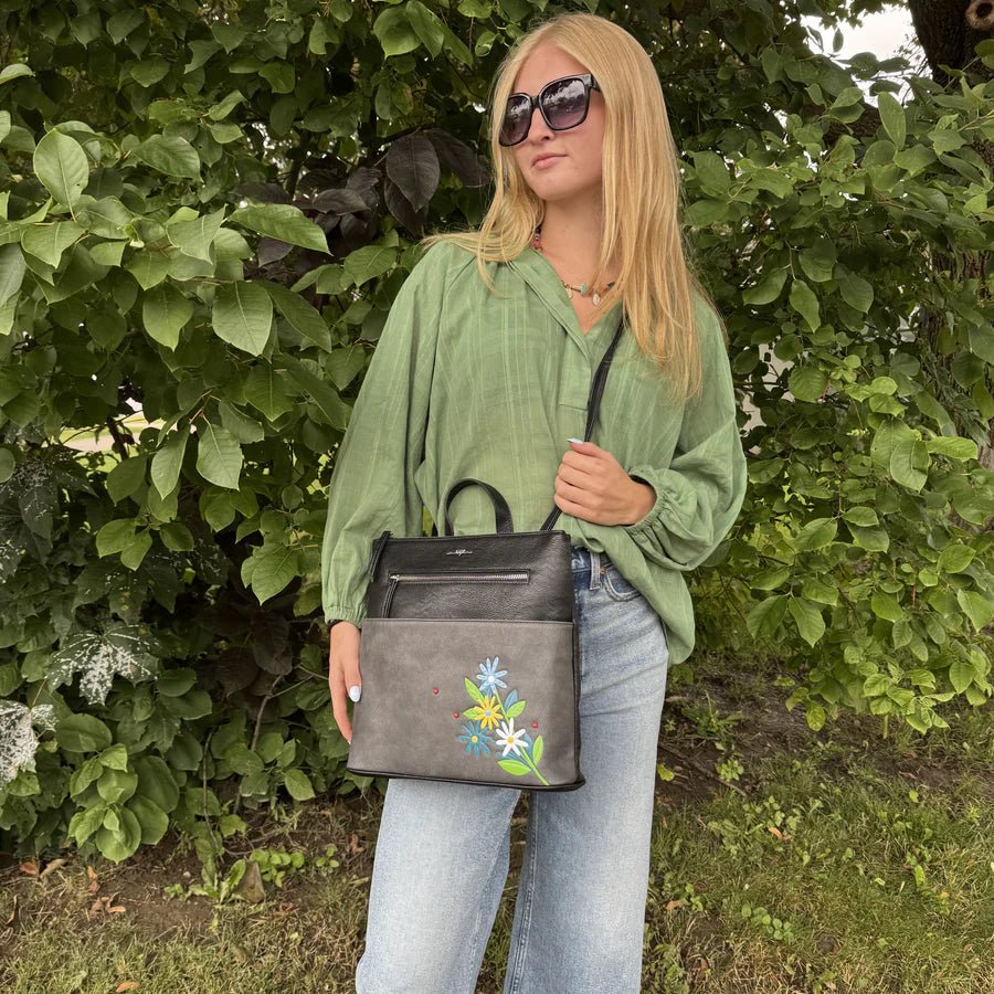 Woman holding a black handbag with floral embroidery in front of green foliage - okotoks hc pharmacy