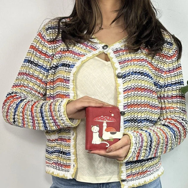 Person wearing a colorful striped jacket holding a red wallet with a cat design. - okotoks hc pharmacy