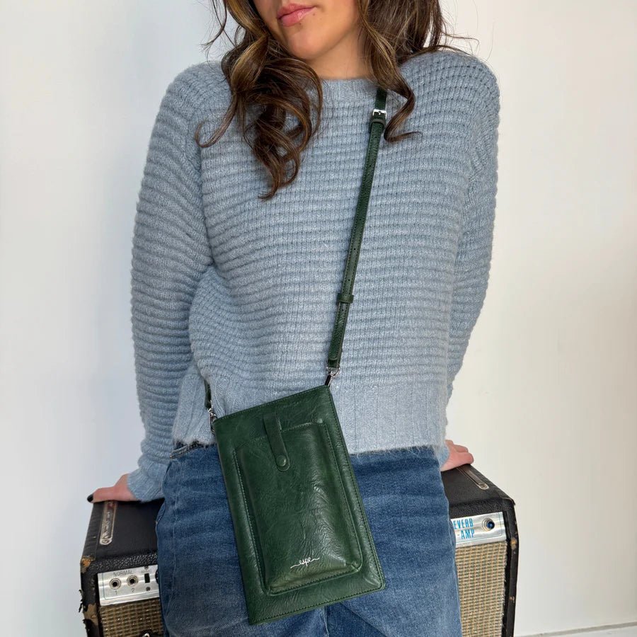 Person wearing a blue sweater and holding a green crossbody bag against a white background - okotoks hc pharmacy