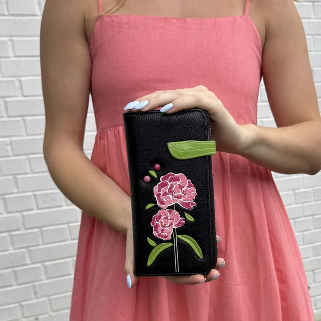 Person holding a black wallet with floral embroidery against a white brick wall. - okotoks hc pharmacy