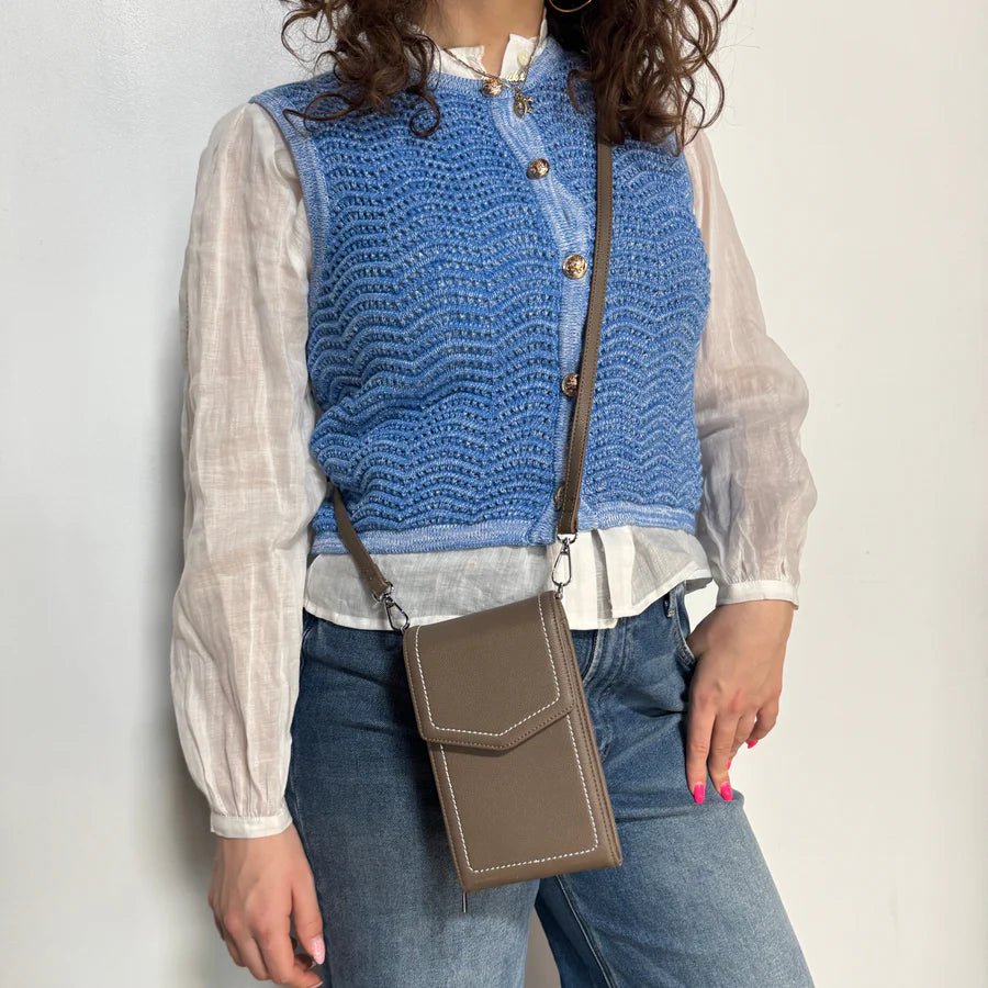 Person wearing a blue knitted vest over a white shirt with a grey crossbody bag. - okotoks hc pharmacy