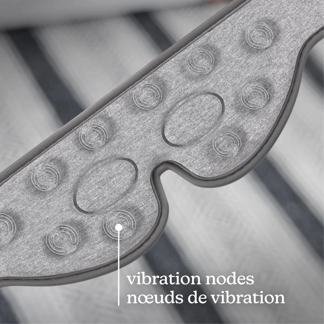 Close-up of a gray textured wearable device with oval and circular vibration nodes, overlaid with the text 'vibration nodes / nœuds de vibration' on a blurred striped background. - okotoks hc pharmacy