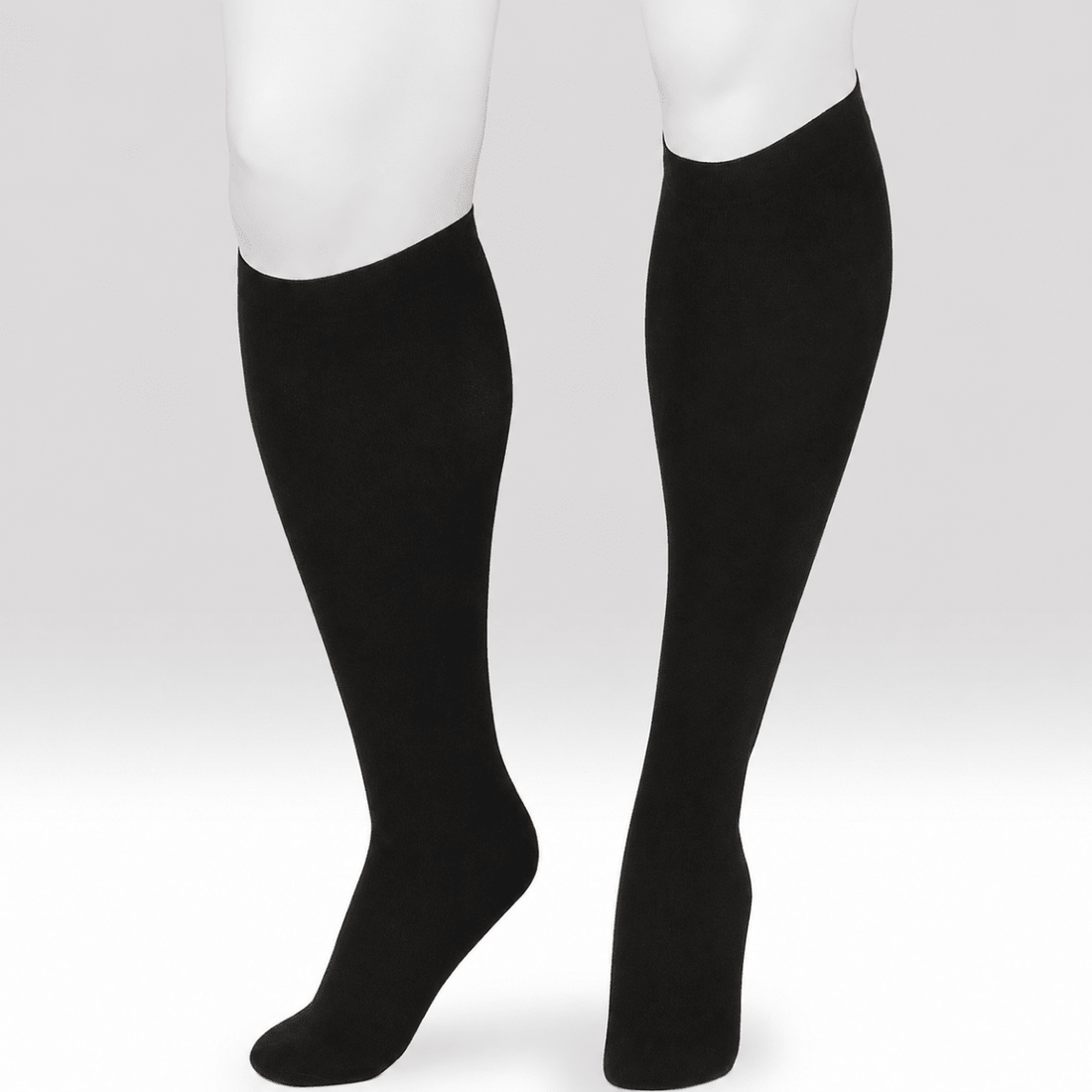 A pair of black knee-high compression socks or calf sleeves shown on a white mannequin lower leg and foot form against a light gray studio background. - okotoks hc pharmacy