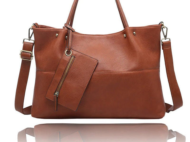 A brown pebbled leather tote bag with dual top handles, a detachable shoulder strap, and a matching zippered pouch hanging from a gold-tone zipper, shown on a white background with a reflection below. - okotoks hc pharmacy