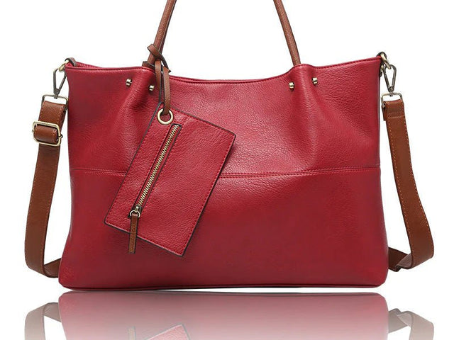 A red faux-leather handbag with brown leather handles, shoulder strap, and zipper pull, shown on a white background with a reflection below. - okotoks hc pharmacy