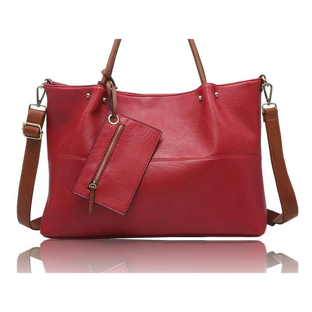 A red faux-leather handbag with brown leather handles, shoulder strap, and zipper pull, shown on a white background with a reflection below. - okotoks hc pharmacy