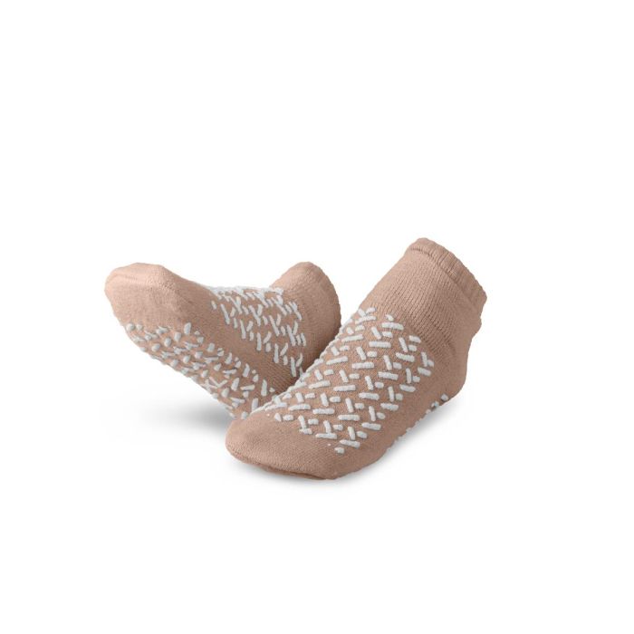 A pair of beige baby socks with white textured grip patterns on the soles and sides, displayed against a clean white background. - okotoks hc pharmacy