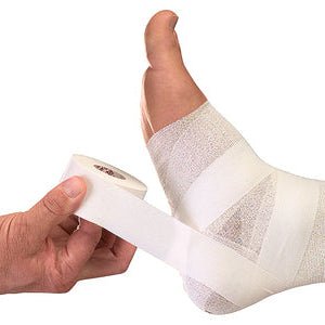 A person's ankle and lower leg are wrapped in white gauze and bandage tape while another hand holds a roll of the same tape against a plain white background. - okotoks hc pharmacy