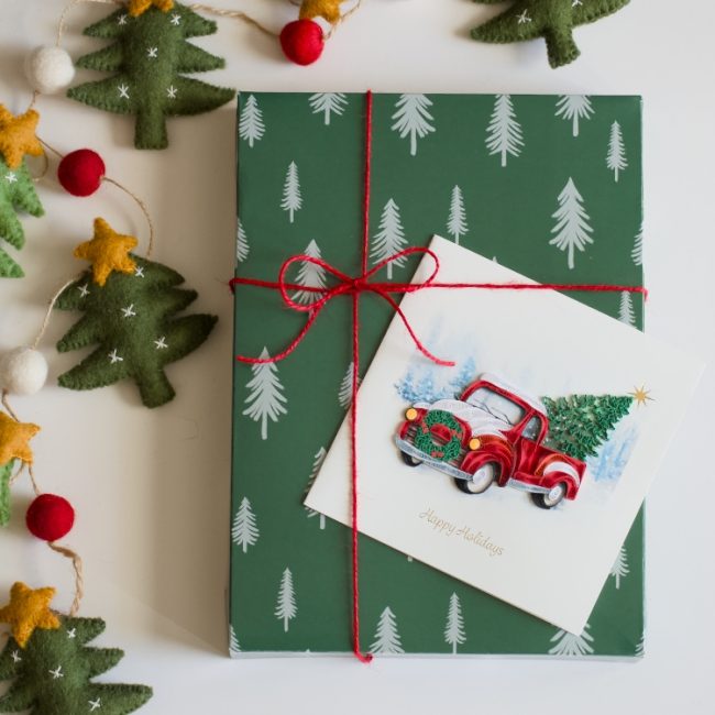 Gift box with Christmas tree pattern and red ribbon, surrounded by festive decorations. - okotoks hc pharmacy
