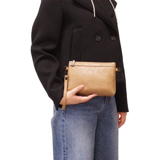 Person holding a beige handbag with a black coat and blue jeans on a white background - okotoks hc pharmacy