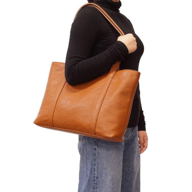 Person holding a brown leather tote bag on a white background - okotoks hc pharmacy