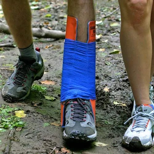 Person wearing a blue cast on one leg with orange accents, standing on a muddy ground. - okotoks hc pharmacy