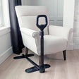 Black adjustable couch cane under a white armchair in a room with light wood flooring and a window. - okotoks hc pharmacy