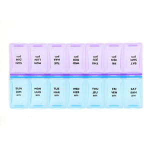 A 7-day weekly pill organizer with translucent plastic compartments. The top row is light purple with black text showing reversed days of the week (SUN, MON, etc. - okotoks hc pharmacy