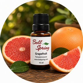 Bell Spring Grapefruit essential oil bottle with a black cap and white label, surrounded by grapefruit slices, a whole grapefruit, and green leaves on a wooden surface with a blurred green background. - okotoks hc pharmacy