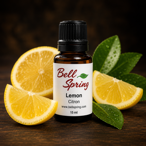 A bottle of Bell Spring Lemon Citron essential oil centered on a dark wooden surface, surrounded by fresh lemon slices and green leaves. - okotoks hc pharmacy