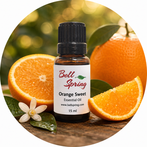 Bell Spring Orange Sweet essential oil bottle with a black cap, set against a circular background of fresh oranges, orange slices, green leaves, and an orange blossom on a wooden surface. - okotoks hc pharmacy