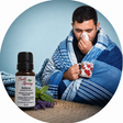 A man wrapped in a blue striped blanket and holding a mug appears in a circular lifestyle scene next to a small Bell Spring Relieve essential oil bottle with lavender sprigs, on a light blue background. - okotoks hc pharmacy