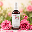 A bottle of Bell Spring Rose Flower Distillate centered on a marble surface, surrounded by fresh pink roses and petals with a soft, blurred garden background. - okotoks hc pharmacy