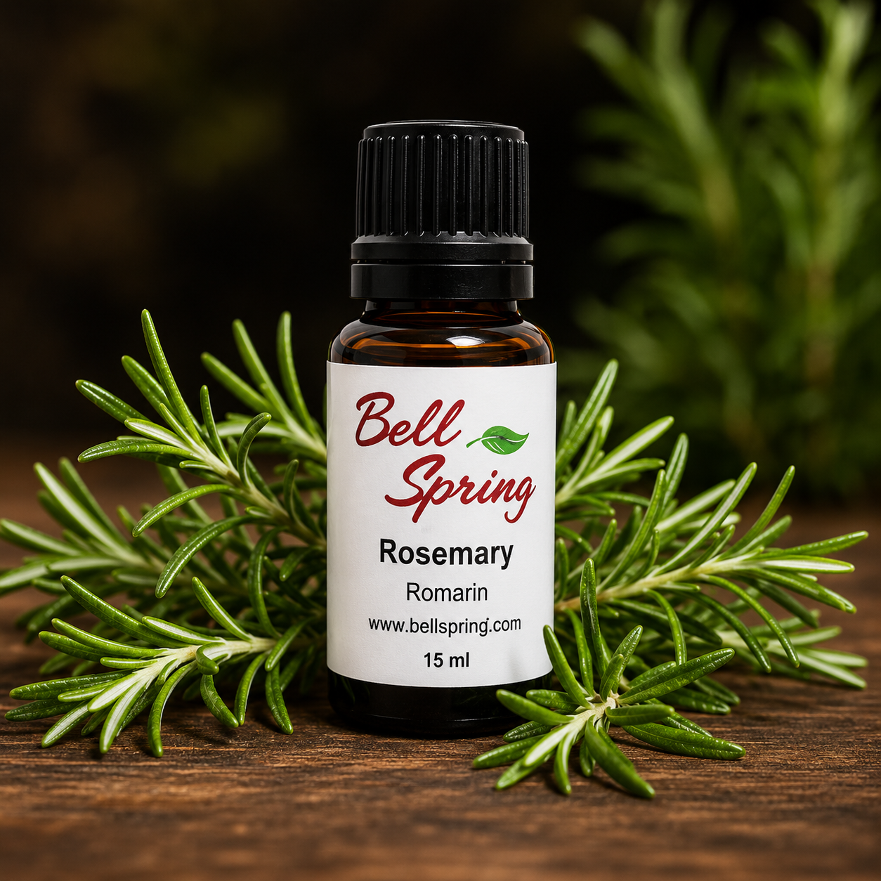A 15 ml bottle of Bell Spring Rosemary essential oil, displayed on a rustic wooden surface and surrounded by fresh green rosemary sprigs. The bottle has a black cap and a white label with red and green text. - okotoks hc pharmacy