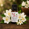 A small amber glass bottle of Bell Spring Sweet Jasmine Doux Jasmin essential oil with a black cap and white label, styled on a wooden surface with white jasmine flowers and green leaves. - okotoks hc pharmacy