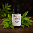 A 15 ml bottle of Bell Spring Tea Tree essential oil, styled with fresh green tea tree leaves on a dark wooden surface against a dark background. - okotoks hc pharmacy
