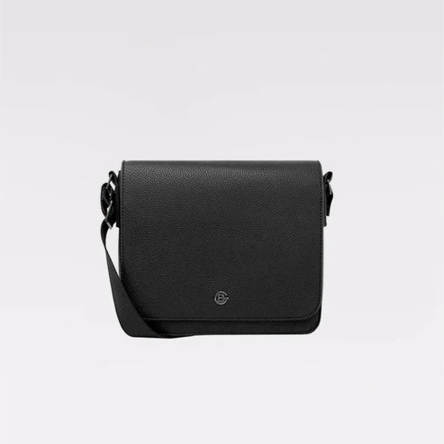 A black pebbled leather crossbody bag with a small circular metal logo emblem on the front flap, displayed against a clean light gray background. - okotoks hc pharmacy