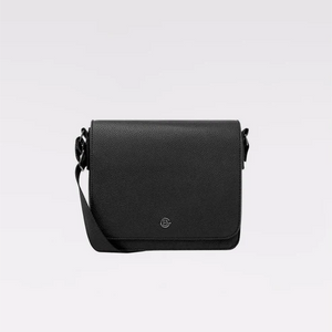 A black pebbled leather crossbody bag with a small circular metal logo emblem on the front flap, displayed against a clean light gray background. - okotoks hc pharmacy