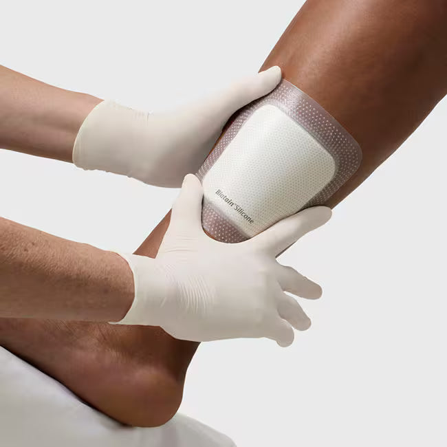 Person applying a bandage to another person's leg with gloved hands on a light background - okotoks hc pharmacy