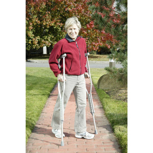 Woman using crutches on a brick path with trees in the background - okotoks hc pharmacy