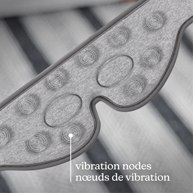 Close-up of a gray textured wearable device with oval and circular vibration nodes, overlaid with the text 'vibration nodes / nœuds de vibration' on a blurred striped background. - okotoks hc pharmacy