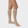 A model's legs wearing beige knee-high compression socks against a light gray background. - okotoks hc pharmacy